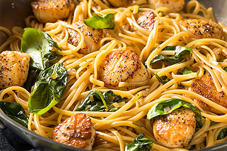 a delicious plate of prepared lemon and garlic pasta with pan-seared scallops is ready to be served.
