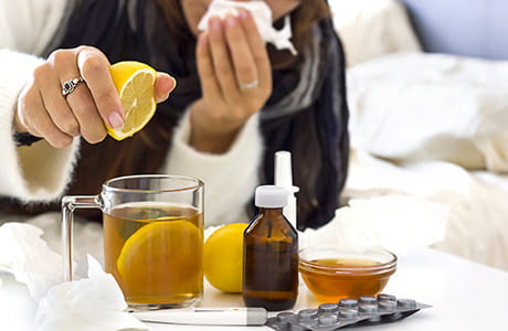 A woman with a cold or flu sitting on the bed and preparing tea with lemon.